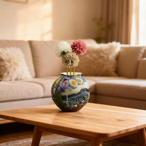 May include: A decorative vase featuring a rendition of Van Gogh's "Starry Night" painting. The vase holds three artificial flowers in shades of pink, white, and tan. The vase is placed on a wooden table in front of a beige sofa.