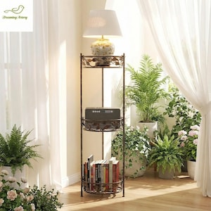May include: A bronze metal floor lamp with three shelves. The top shelf holds a lamp with a white shade. The middle shelf has a speaker, and the bottom shelf holds books. The shelves have a decorative leaf design.
