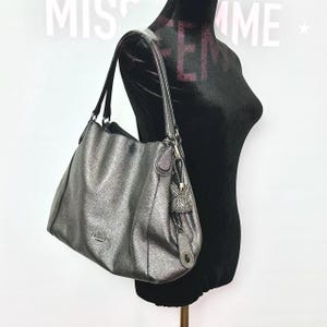 Cartera gris metalizada de Coach, años 2000. Tiene un pequeño desgaste vintage en la parte posterior (que se muestra en las fotos). Incluye un llavero de conejo.