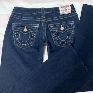 Puede incluir: Vaqueros de mezclilla azul oscuro con un dise&ntilde;o cl&aacute;sico de cinco bolsillos. Incluye costuras decorativas, cierre de bot&oacute;n y cremallera, y la etiqueta de la marca True Religion en la parte trasera. Los vaqueros tienen una abertura de pierna acampanada.