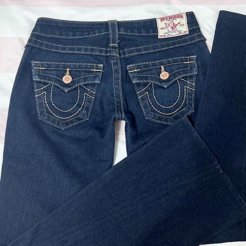 Puede incluir: Vaqueros de mezclilla azul oscuro con un dise&ntilde;o cl&aacute;sico de cinco bolsillos. Incluye costuras decorativas, cierre de bot&oacute;n y cremallera, y la etiqueta de la marca True Religion en la parte trasera. Los vaqueros tienen una abertura de pierna acampanada.