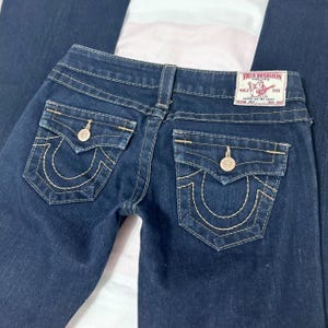 Puede incluir: Vaqueros de mezclilla azul oscuro con un dise&ntilde;o cl&aacute;sico de cinco bolsillos. Cuenta con costuras decorativas en los bolsillos traseros y una etiqueta True Religion. Los vaqueros tienen cierre de bot&oacute;n y cremallera.