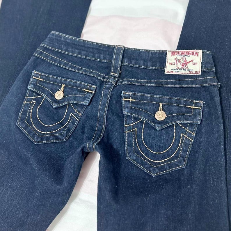 Puede incluir: Vaqueros de mezclilla azul oscuro con un dise&ntilde;o cl&aacute;sico de cinco bolsillos. Cuenta con costuras decorativas en los bolsillos traseros y una etiqueta True Religion. Los vaqueros tienen cierre de bot&oacute;n y cremallera.