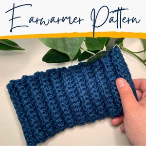May include: A close-up of a dark blue crocheted ear warmer. The ear warmer is made with a textured stitch and is lying on a white surface.