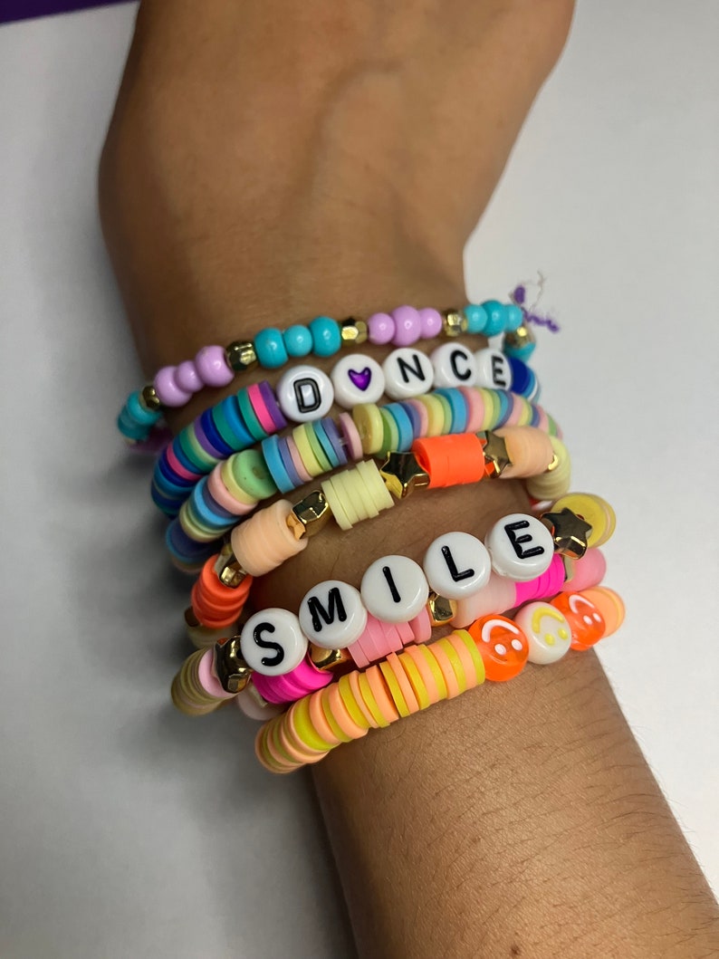 May include: A stack of colourful beaded bracelets with letter beads spelling out "DANCE" and "SMILE". The bracelets also feature heart, star and smiley face beads.