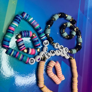 May include: Three colourful beaded bracelets with the words "Don't Smile" and "Emo" spelled out in white letters. The bracelets are made of small, round beads in various colours, including blue, pink, yellow, and white.