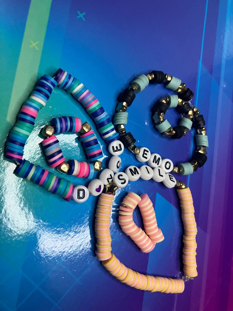 May include: Three colourful beaded bracelets with the words "Don't Smile" and "Emo" spelled out in white letters. The bracelets are made of small, round beads in various colours, including blue, pink, yellow, and white.