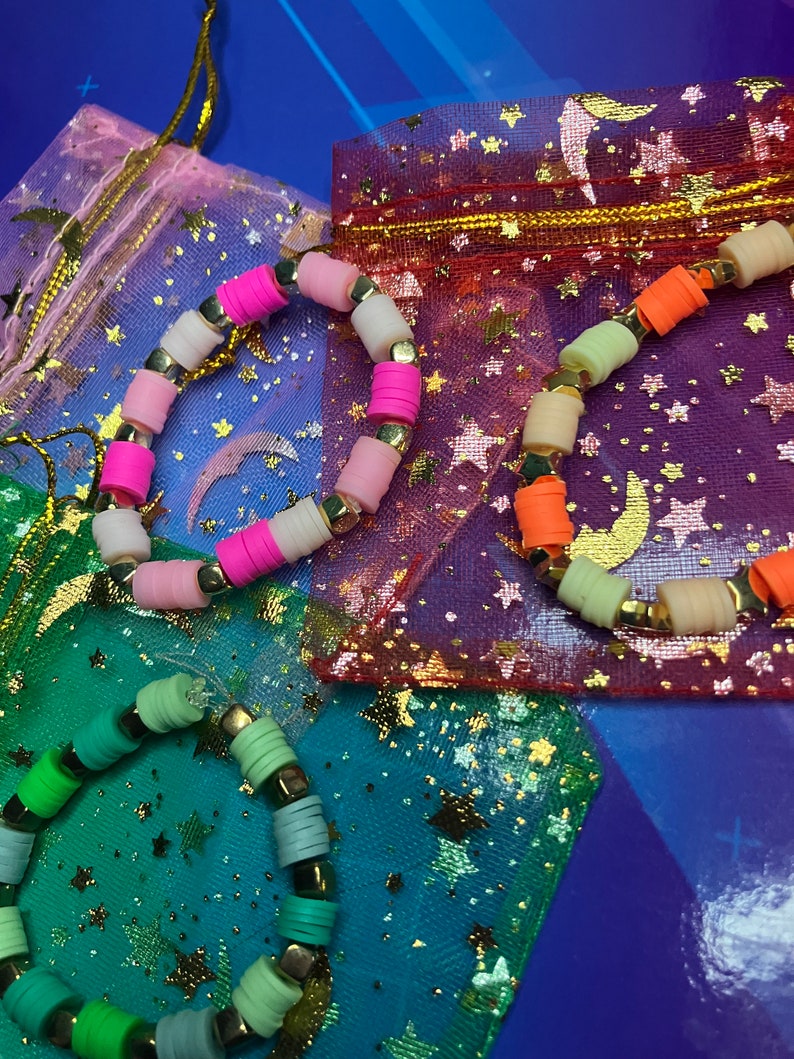 May include: Three colourful beaded bracelets with gold accents, displayed on star-patterned fabric bags.