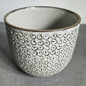 May include: A white ceramic bowl with a brown rim and a black and white speckled pattern.