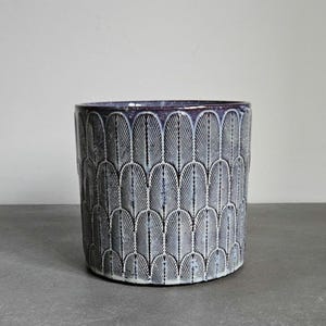 May include: A ceramic planter with a white and purple geometric pattern. The planter is cylindrical and has a smooth, glazed finish.