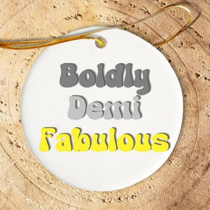 May include: White ceramic ornament with the text "Boldly Demi Fabulous" in gray and yellow lettering.