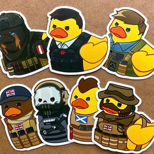 May include: Set of eight rubber ducky figurines, each dressed in a different military uniform. The ducks are yellow with black eyes and orange beaks. Each duck is wearing a different camouflage pattern and has a different military insignia on their chest.