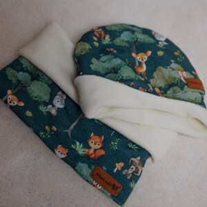 Könnte beinhalten: Ein blaues und weißes Baby-Mützen- und Schals-Set mit einem Waldtier-Druck. Die Mütze hat ein weißes Fleece-Futter und der Schal hat ein braunes Leder-Etikett mit dem Text "Made with Love".