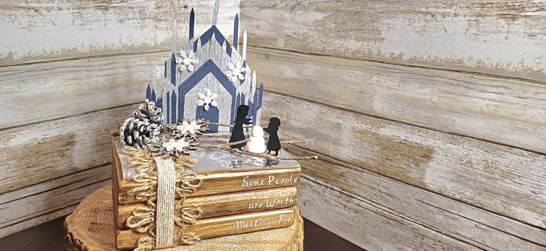 May include: A stack of four books with a winter-themed design. The top book has a blue and white paper castle on top. The books are wrapped in twine and have the text "Some People are Worth Melting For" on the front.