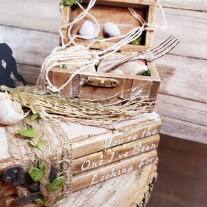 K&ouml;nnte beinhalten: Eine Holzkiste mit rustikalem Design, verziert mit Muscheln, Schnur und einer Gabel. Die Kiste ist auf einer kleineren Holzkiste mit dem Text "You're the One I've Been Looking For" gestapelt.