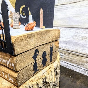 May include: A wooden tiered display with a black silhouette of a gate, a tombstone, and a crescent moon. The display is decorated with the text "We're simply meant to be."