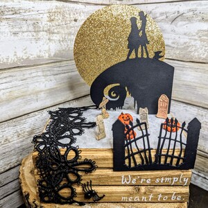 May include: A black and white silhouette of Jack Skellington and Sally from the Nightmare Before Christmas movie, standing on a hilltop with a golden moon behind them. The scene is set in a graveyard with a gate, tombstones, and pumpkins. The text "We're simply meant to be." is written below the image.