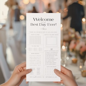 May include: A white wedding activity card held by hands, featuring the text "Welcome to the Best Day Ever!" and various games like Four in a Row, Tic-Tac-Toe, and a word search. The card includes a photo scavenger hunt and is dated September 28, 2025.