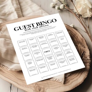 K&ouml;nnte beinhalten: Eine schwarz-wei&szlig;e druckbare Bingokarte mit dem Titel "Guest Bingo: Book Club Edition". Die Karte hat 25 Felder mit verschiedenen buchbezogenen Aktivit&auml;ten, wie z. B. "Besitzt einen zu gro&szlig;en TBR-Stapel", "Liebt Bibliotheksverk&auml;ufe", "Hat "noch ein Kapitel" gesagt und gelogen", "Hat ein Buch an einem Tag beendet", "Ist beim Lesen eingeschlafen", "Bevorzugt physische B&uuml;cher", "Hat ein seltsames Lesezeichen verwendet", "Hat ein Buch versehentlich ruiniert", "War von einer &uuml;berraschenden Wendung geschockt", "Liebt Theorien &uuml;ber B&uuml;cher", "Hat ein Buch nach dem Einband beurteilt", "Kann ein Buch nicht unvollendet lassen", "Denkt, dass B&uuml;cher besser sind als Filme", "Hat den Namen einer Hauptfigur vergessen", "Kauft B&uuml;cher, liest sie aber nie", "Liest mehrere B&uuml;cher gleichzeitig", "Hat ein Buch ins Wasser fallen lassen", "Hat einen Autor getroffen", "Bringt &uuml;berall ein Buch mit", "Liebt den Geruch von B&uuml;chern", "Ist nach 2 Uhr morgens wach geblieben und hat gelesen", "Liest Taschenb&uuml;cher".