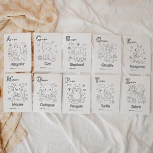 May include: A set of ten white cards with black line drawings of animals, each labeled with a letter of the alphabet. The animals include an alligator, cat, elephant, giraffe, kangaroo, mouse, octopus, penguin, turtle, and zebra. A wooden toy is on the right.
