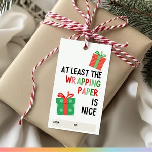 May include: White gift tag with red and green illustrations of wrapped presents. The text reads "At least the wrapping paper is nice." with blank spaces for "From:" and "To:".