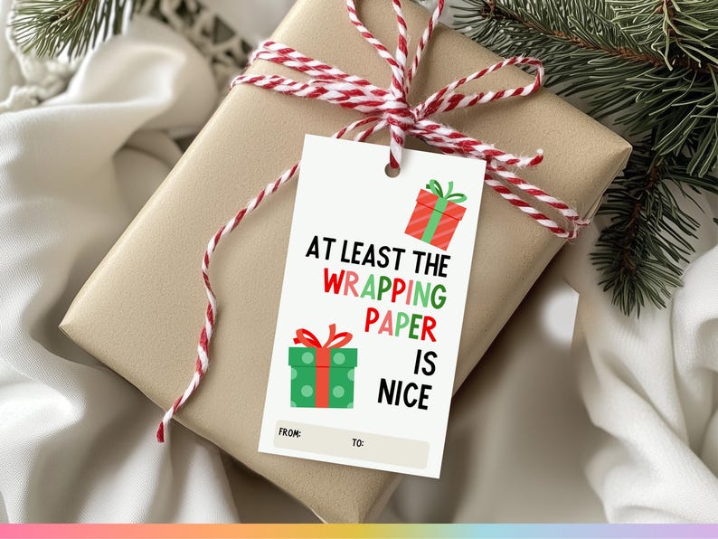 May include: White gift tag with red and green illustrations of wrapped presents. The text reads "At least the wrapping paper is nice." with blank spaces for "From:" and "To:".