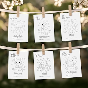 May include: Six white cards with black line drawings of animals and objects, each card is held by a wooden clothespin. The cards feature a jellyfish, kangaroo, lion, mouse, nest, and octopus. Each card has the letter of the alphabet and the word for the image.