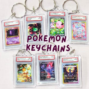 Może przedstawiać: Kolekcja breloków Pokemon z różnymi kartami kolekcjonerskimi Pokemon w przezroczystych plastikowych uchwytach. Breloki mają srebrne metalowe kółka. Tekst "Pokemon Keychains" jest wyświetlany na środku.