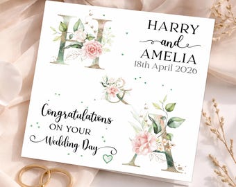Puede incluir: Una tarjeta de boda blanca con anillos dorados en primer plano. La tarjeta presenta los nombres "Harry y Amelia" y la fecha "18 de abril de 2026". También hay diseños florales y las palabras "Felicitaciones en tu día de boda".