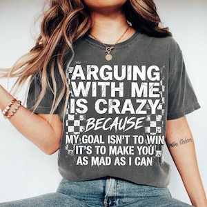 May include: Dark gray t-shirt with the text "ARGUING WITH ME IS CRAZY BECAUSE MY GOAL ISN'T TO WIN IT'S TO MAKE YOU AS MAD AS I CAN" in white. The shirt has a distressed, vintage look.