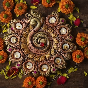 Könnte beinhalten: Ein dekorativer, bronzefarbener Kerzenhalter im Pfauendesign mit brennenden Kerzen. Der Halter ist von orangefarbenen Ringelblumen und Blütenblättern umgeben, die auf einer dunklen Holzoberfläche liegen.