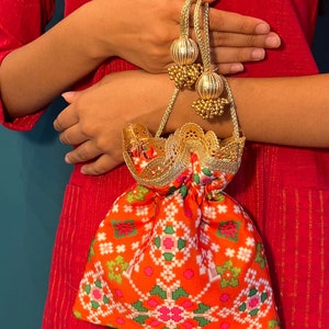 May include: A small orange and white patterned drawstring bag with gold trim and tassels. The bag is made of fabric and has a delicate lace trim.