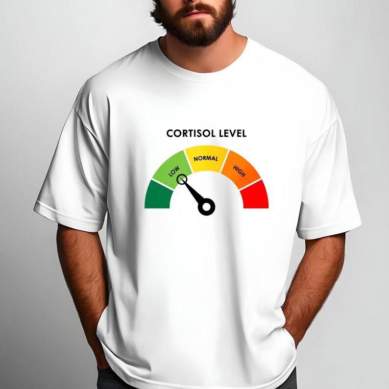 Puede incluir: Camiseta blanca con un gr&aacute;fico de un medidor de nivel de cortisol. El medidor tiene una aguja que apunta a la secci&oacute;n "bajo", con secciones codificadas por colores verde, amarillo y rojo. El texto "CORTISOL LEVEL" est&aacute; encima.