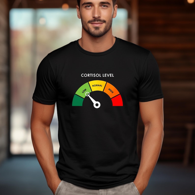 Puede incluir: Camiseta negra con un gr&aacute;fico de medidor de nivel de cortisol. El medidor muestra un espectro de verde (bajo) a rojo (alto), con "Normal" en amarillo. El texto "CORTISOL LEVEL" est&aacute; encima del medidor. Una camiseta casual.