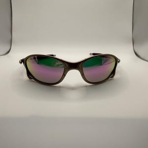May include: A pair of sunglasses with a dark brown frame and iridescent lenses that reflect shades of pink, green, and purple. The sunglasses have a curved design and are set against a white background.