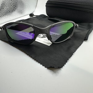 May include: A pair of black sunglasses with green and purple mirrored lenses. The sunglasses are on a black microfiber cloth with a small white tag that reads "Tyler Duncan Handmade, 82 Paper Street, Ford, 19808".