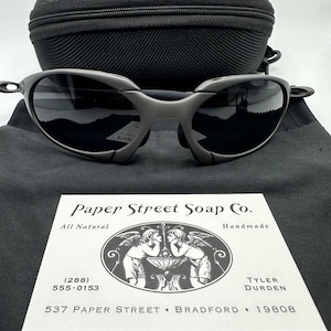 May include: A business card for Paper Street Soap Co. with a black and white illustration of two angels holding a bowl. The card includes the company name, address, phone number, and the text "All Natural" and "Handmade".