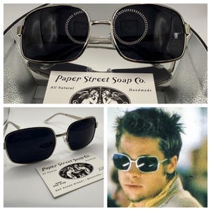 May include: Silver framed square sunglasses with black lenses. The sunglasses are shown in a close-up view and also worn by a person. The image includes the text "Paper Street Soap Co. All Natural Handmade".