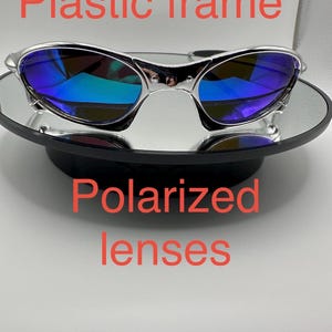 Op de afbeelding: Zonnebril met een zilverkleurig kunststof montuur en gepolariseerde glazen. De glazen hebben een blauwgroene reflecterende coating. Tekst op de afbeelding luidt "Kunststof montuur" en "Gepolariseerde glazen".