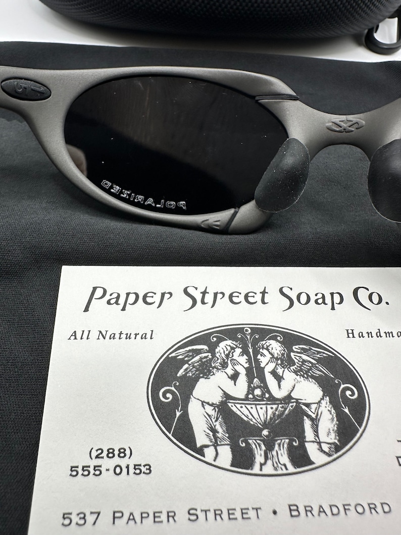 May include: A white card with black text and a black and white illustration of two angels. The text reads "Paper Street Soap Co. All Natural Handmade (288) 555-0153 537 Paper Street Bradford"