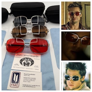 May include: Three pairs of rectangular sunglasses with silver frames and lenses in red, brown, and black. Includes black protective cases, light blue cleaning cloths, and two business cards for Paper Street Soap Co. and FMC Recall Coordinator.