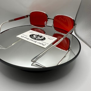 May include: Silver framed sunglasses with red lenses. The sunglasses are sitting on a mirrored surface with a business card for "Paper Street Soap Co." in the background.