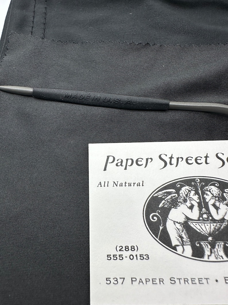 May include: A white business card with black text that reads "Paper Street So", "All Natural", "(288)", "555-0153", and "537 PAPER STREET E". The card features a black and white illustration of two angels.