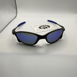 May include: Black sunglasses with blue mirrored lenses and blue temple tips. The sunglasses have a sleek, modern design. A business card with the text "Paper Street Soap Co." is behind the sunglasses.
