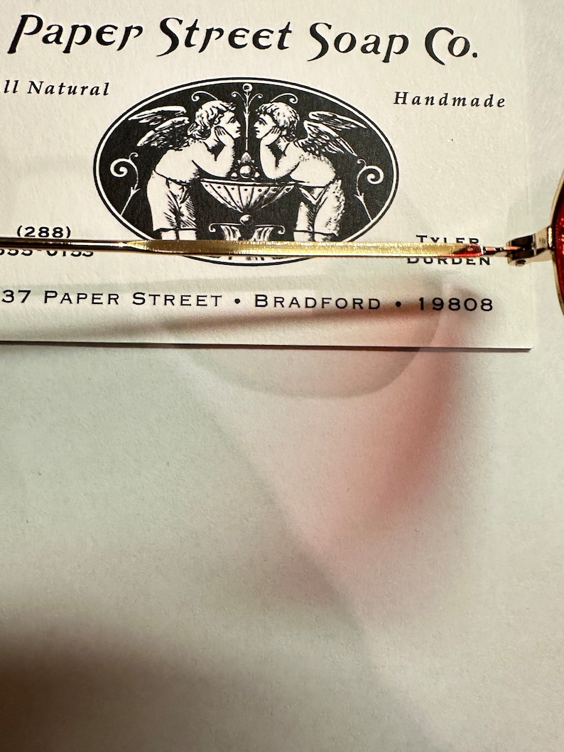 Może przedstawiać: Wizyt&oacute;wka firmy Paper Street Soap Co., producenta ręcznie robionego mydła. Na wizyt&oacute;wce znajduje się czarno-biała ilustracja dw&oacute;ch anioł&oacute;w z skrzydłami, logo i adres firmy: 37 Paper Street, Bradford, 19808.