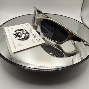 Peut inclure: Des lunettes de soleil &agrave; monture argent&eacute;e et verres fonc&eacute;s reposent sur une surface miroir. Une carte de visite pour "Paper Street Soap Co." est &eacute;galement sur le miroir. Les lunettes de soleil ont un design &eacute;l&eacute;gant et moderne.