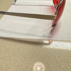 Puede incluir: Gafas de sol con montura plateada y lentes tintados de rojo. Las gafas est&aacute;n inclinadas para mostrar el perfil lateral.