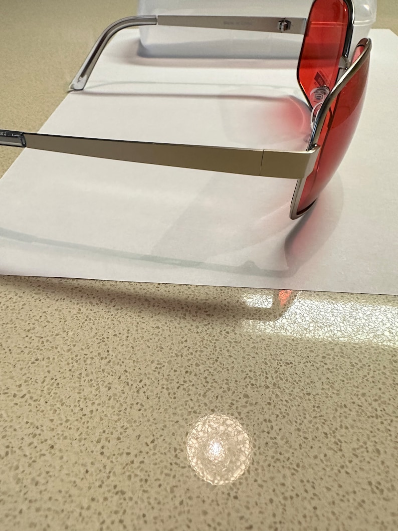 Puede incluir: Gafas de sol con montura plateada y lentes tintados de rojo. Las gafas est&aacute;n inclinadas para mostrar el perfil lateral.