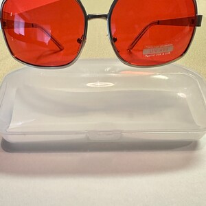 Puede incluir: Gafas de sol con montura plateada y lentes rojas. Las gafas tienen una etiqueta que dice "100% Eye Protection UV400 Against UVA & UVB".