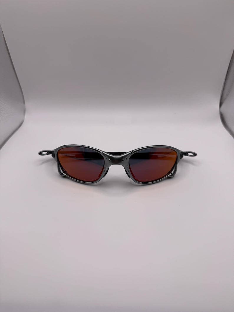 May include: A pair of sunglasses with a dark gray metal frame and reddish-orange lenses. The sunglasses have a sleek, modern design, suitable for outdoor activities. The lenses provide protection from the sun's glare.